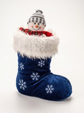 A festive blue christmas stocking decorated with white snowflakes features a cute plush snowman toy peeking out from the top against a plain white background