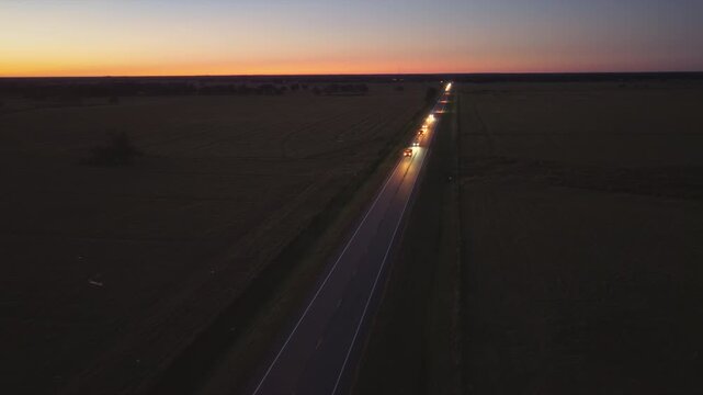 Cars driving along a straight road through open land, headlights cutting through dusk, symbolizing direction, journey and destination.