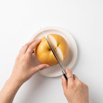 Hands slicing giant Korean Asian pear with knife isolated on pure white background