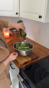person mixes a bowl of vegetables with tongs, adds oil, and seasons it with salt