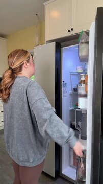 woman opens fridge and can't decide what to eat