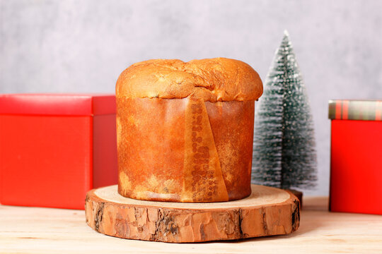 Golden Christmas panettone on a wooden stand on a table, with gifts and a Christmas tree in the background and space for text.