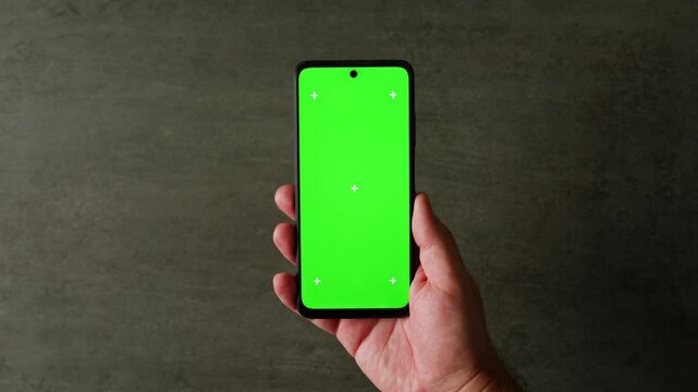 Hand holding phone with chroma key green screen, mockup mobile phone at modern office closeup, businesswoman reading work message on green screen smartphone at workplace. 