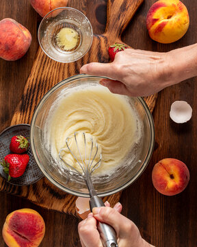 Hands vigorously stirring batter for making a strawberry peach cake. 