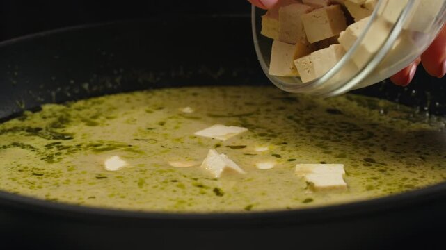 Green curry tofu soup cooking. Thai green curry soup in a white bowl on a white plate with dark background. Flat lay, overhead