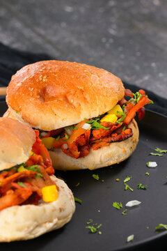 Close-up of a juicy al pastor pork bun or cemita with ingredients and condiments on a rustic dark surface
