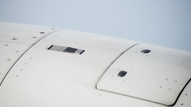 Close up cinematic panning shot of white airplane wing surface with bolts and fasteners during flight.