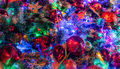 Naklejka premium Close up of colorful Christmas tree illuminated with glowing LED lights, red baubles, glitter ornaments and evergreen branches creating festive background for holiday and New Year celebrations.
