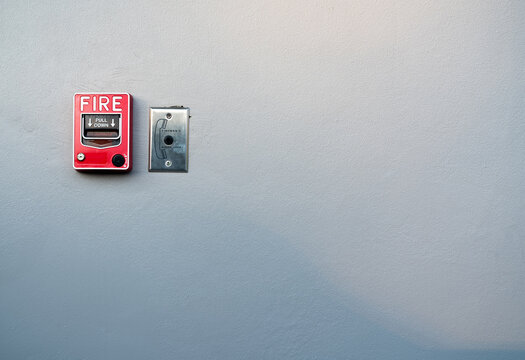 Fire alarm pull station mounted on white concrete wall with copy space, emergency warning equipment for fire safety systems in schools, hospitals, offices, factories, apartments and public buildings.