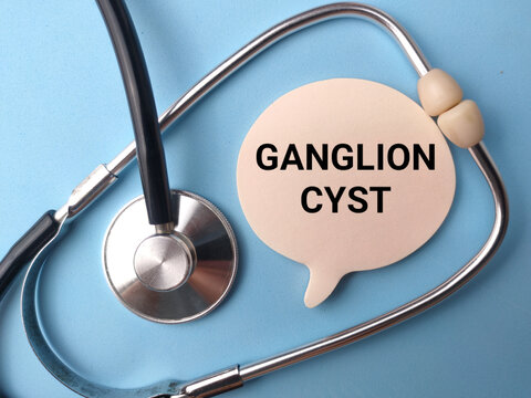 A speech bubble paper cutout labeled GANGLION CYST rests inside the loop of a stethoscope on blue