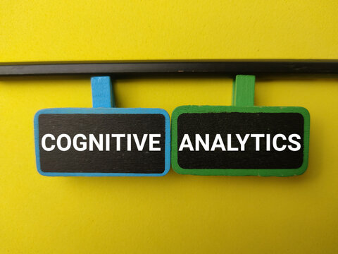 Two small blackboards displaying COGNITIVE and ANALYTICS hang from clips against a bright yellow background