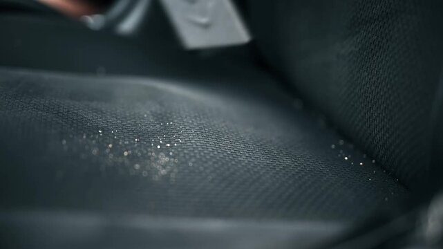 Professional car detailing service vacuuming dust from black vehicle fabric interior seat upholstery.