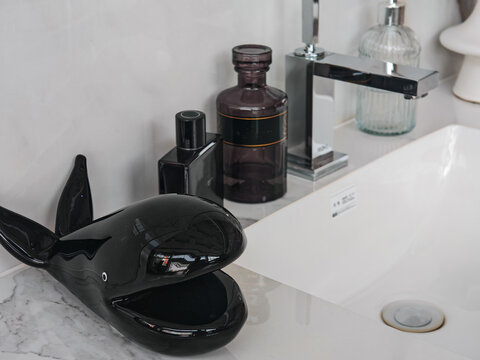 modern bathroom vanity counter featuring white ceramic sink basin, chrome mixer faucet, luxury fragrance bottles, and black decorative ceramic sculpture, ideal for interior staging catalogs, hotel lux
