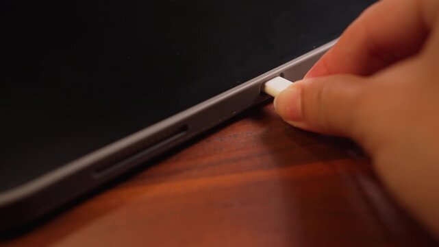 Extreme macro shot of hand plugging white cable into tablet side port as dark screen turns bright green screen, chroma key display and digital hardware concept.