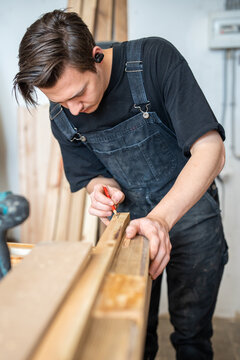 Skillful craftsman restorer engaged in process or repairing old wooden window frame in restoration workshop, joiner attentively checking and comparing fitting of wooden boards replacement at workbench