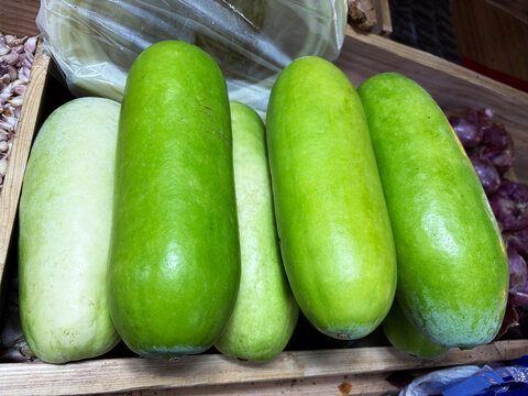 Fresh winter melons and ash gourds arranged in wooden crate at local Asian market