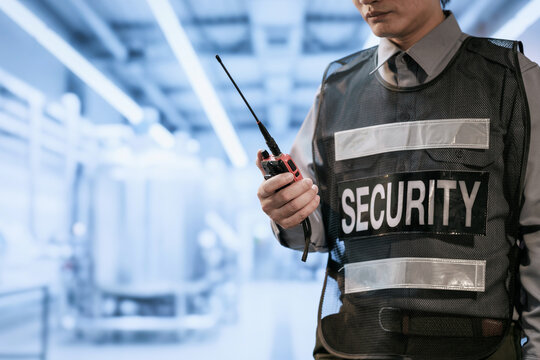 Close view of a uniformed security guard holding a two-way radio in a bright modern building corridor.