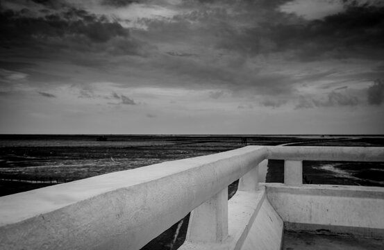 Black and white scene of mud beach at tide with grey sky and clouds. Perspective view from concrete bridge. Depressed, hopeless, despair, grief, lament, sad, and death concept. Loneliness life.