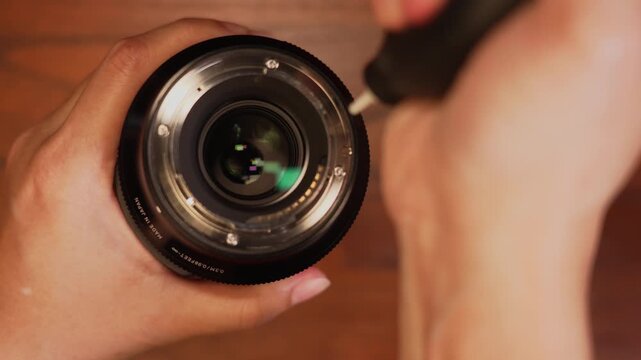 Top view shot of hand holding camera lens on left frame leaving copy space while using air blower on rear element, optics maintenance concept.