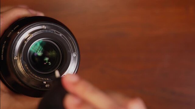 Extreme close up shot of hand tilting camera lens and using rubber air blower to clean dust from rear element, camera gear maintenance concept.
