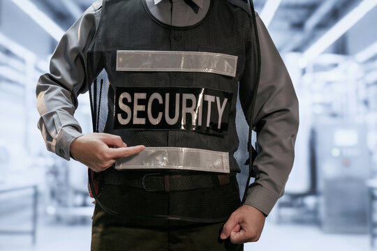 Close-up of a security guard in uniform wearing a protective vest and pointing at the word security in a bright modern building.