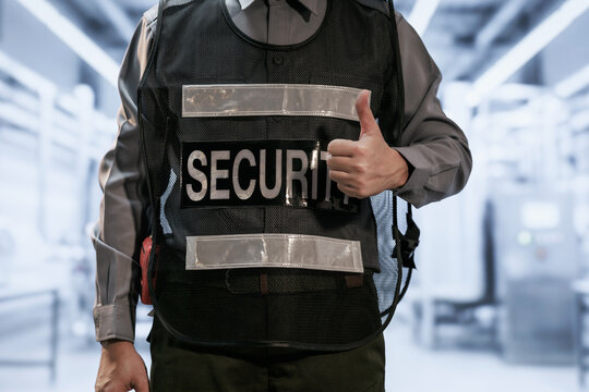 Close-up of a uniformed security guard wearing a protective vest and giving a thumbs-up in a modern indoor public building.