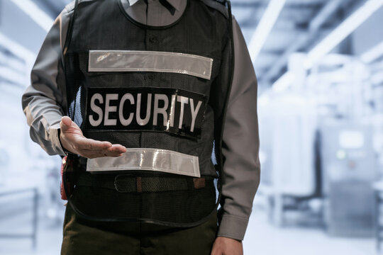 Close view of a security guard in a black protective vest with an outstretched hand inside a modern airport or public building.