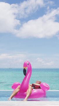 Travel vacation holidays concept. Woman in pool by beach sunbathing in bikini in inflatable pink flamingo toy mattress float relaxing in luxury. Raw vertical video of real woman model without makeup