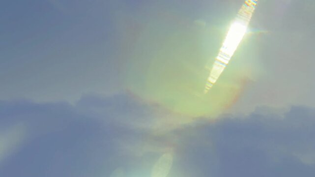 Bright sun shining through blue clouds creating radiant light flares across the vast sky with lens flares stretching vast clear daylight