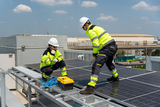 Solar engineers installing photovoltaic panels on commercial rooftop, Worker team in high visibility jackets mounting solar power system, Technicians working on rooftop solar panel installation