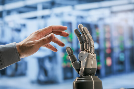 Human hand reaching toward a raised robotic hand in a blurred modern laboratory, connection between people and artificial intelligence.