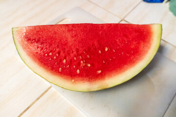 Bright red watermelon resting on a white cutting board. This juicy fruit features striking reddish pink flesh. © Joshua Prasetyadi