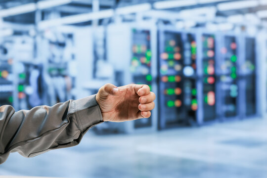 Close-up of a technician's hand reaching in a modern industrial control room with blurred electrical panels and glowing indicator lights.