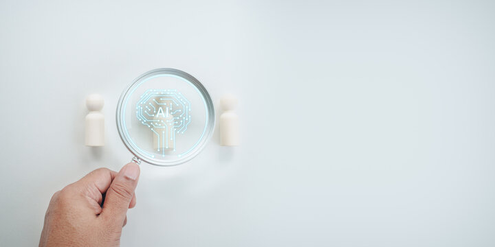Hand holding magnifying glass focusing with artificial intelligence AI brain circuit icon on wooden peg doll figures, white background, concept of AI technology search and human resource management.
