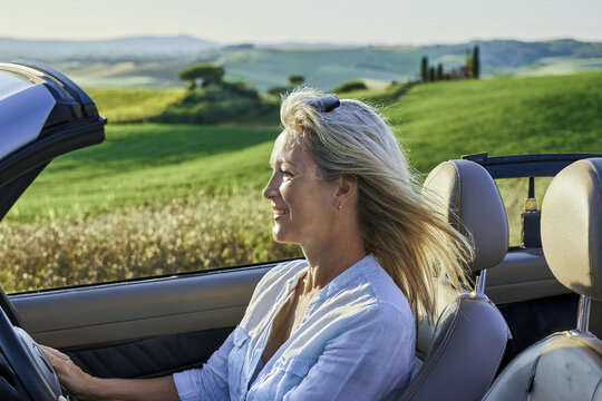 happy woman enjoys driving a convertible in beautiful landscape