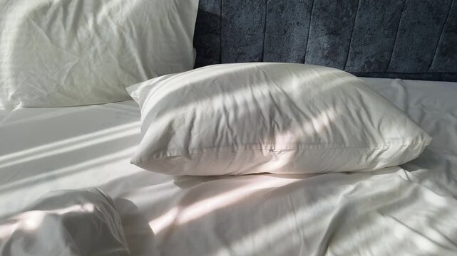 Close-Up motion above Empty Disheveled Bed with White Pillows Against Blue Velvet Headboard in Soft Morning Light