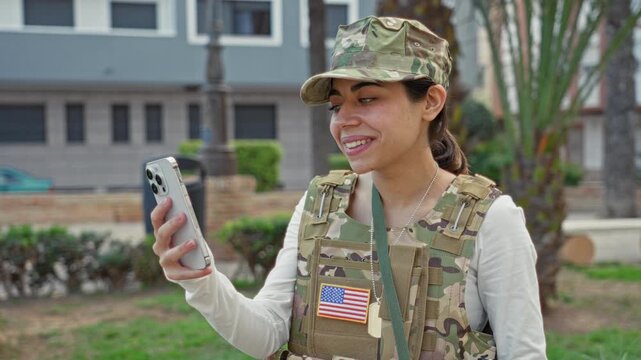 Woman soldier holding smartphone with hand, looking at screen and wearing us flag patch on uniform in street; pride duty.