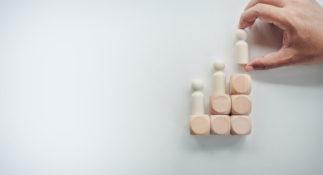 Hand placing wooden peg doll figure on top of staircase blocks chart on white background, concept of business growth, career promotion, leadership development, and success strategy.