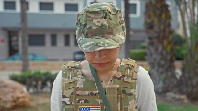 Woman in military uniform with visible eyes looking at camera in building, wearing camo cap and tactical vest with us flag patch and dog tag; duty resolve.