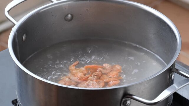 Close-up of adding dried shrimp into a pot of boiling water with glass noodles, preparing ingredients for Thai spicy glass noodle salad (Yum Woon Sen)