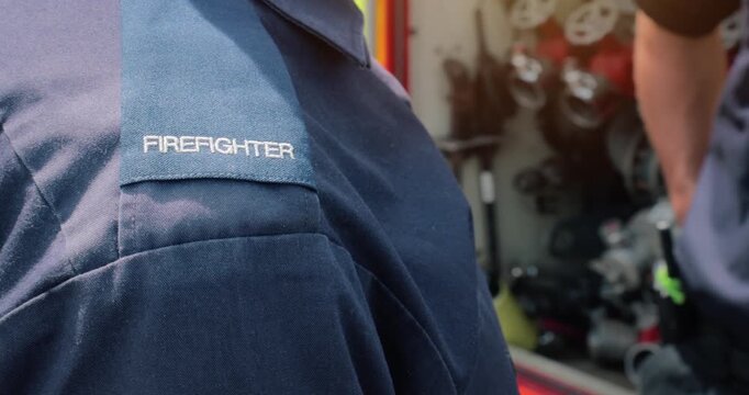 Firefighter team - firemen equipped with emergency services response firefighting crew uniform and gear near fire engine. Department red fire truck appliance from fire station is in scene background.