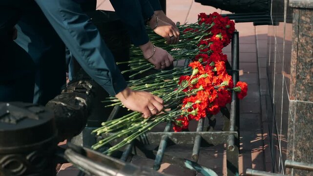 Close-up of people laying red carnations at a memorial during a remembrance ceremony, honoring the memory of fallen people with flowers.