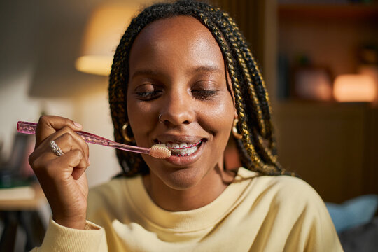 African American girl brushing teeth with braces, smiling during morning routine. Image ideal for dental hygiene campaigns and orthodontic care marketing, close up shot