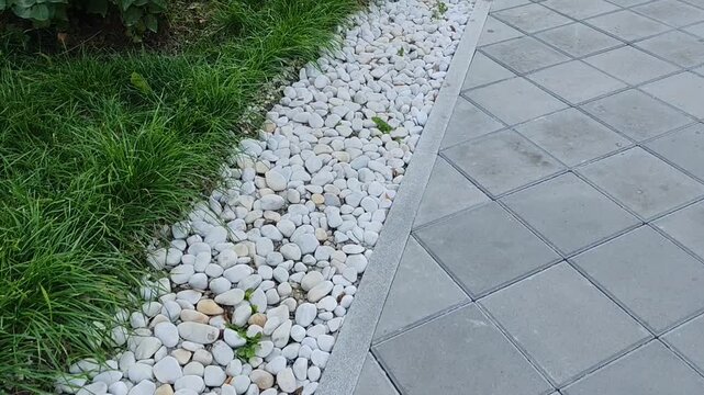 Landscaped garden with white pebbles and green grass on a tiled walkway.
