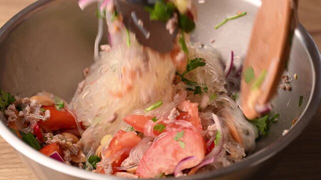 Close-up of mixing Thai spicy glass noodle salad (Yum Woon Sen) in a mixing bowl, preparing delicious Thai food