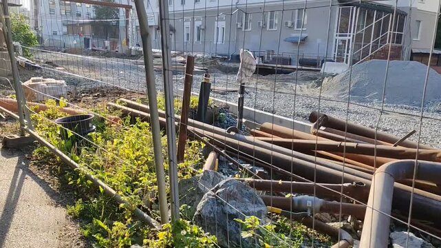 Construction site with debris and overgrown plants under sunlight