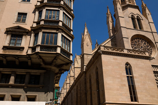 Ornate historic building facade with balcony beside gothic spires and rose window of La Seu cathedral in Palma, Mallorca, Spanish architecture scene