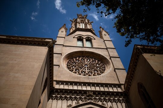 Low angle view of gothic tower with rose window of La Seu cathedral in Palma, Mallorca, ornate stone architecture against blue sky