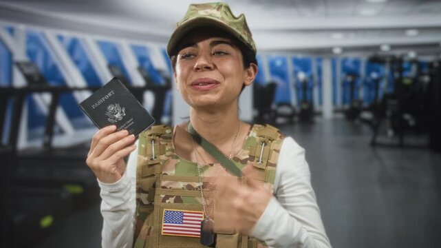 Woman soldier holding passport in hand inside building, smiling with hand over chest and american flag patch visible; pride duty.