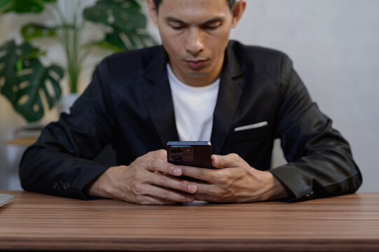 Man in Black Suit Using Smartphone at Modern Desk with Plants